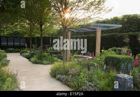 Un jardin moderne au lever du soleil avec un chemin de jardin contemporain et des bordures herbacées de plantation mixte et pergola UK Banque D'Images