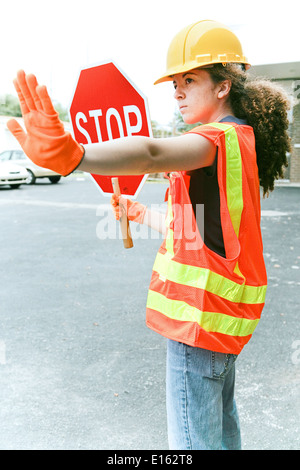 Young female construction apprenti tenant un panneau stop et diriger la circulation. Banque D'Images