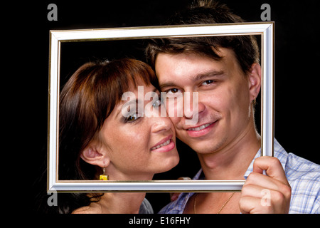 Couple heureux dans l'image. Beau jeune couple à la recherche grâce à un cadre photo et souriant sur noir