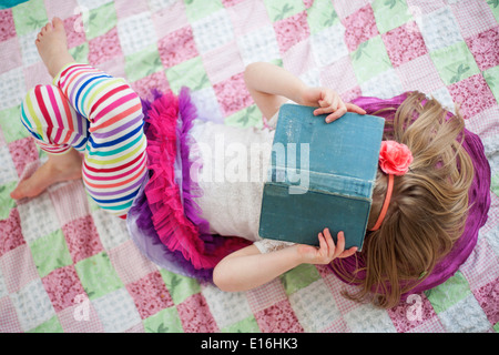 Girl (4-5) reading book allongé sur le dos à la maison Banque D'Images