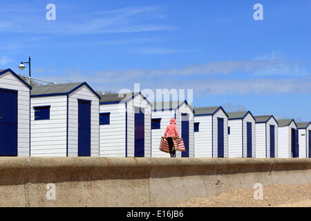 Southwold, Suffolk, Angleterre, Royaume-Uni. 24 mai 2014. Il s'agissait d'une lumineuse journée sur la côte du Suffolk au début de la Banque week-end de vacances. Une dame portait deux transats rayé rouge à côté des cabanes de plage sur le front de mer. Banque D'Images