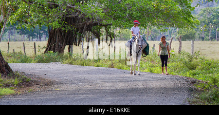 Un jeune garçon sur un cheval et une jeune fille marche chat sur une paisible route de campagne à travers la péninsule d'Osa au Costa Rica Banque D'Images