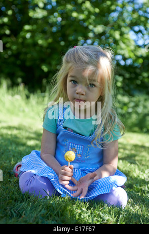 Petit enfant blond girl licking lollipop en extérieur dans jardin, portrait Banque D'Images