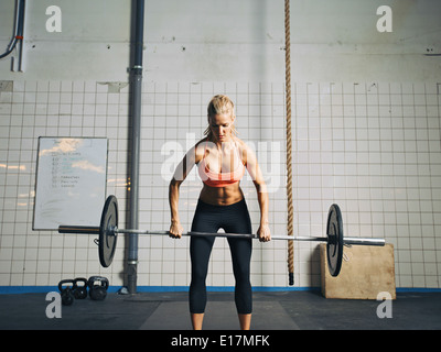 Mettre en place et attractive caucasian female tenant un barbell dans ses mains. Femme Crossfit poids lourds de levage en salle de sport. Banque D'Images