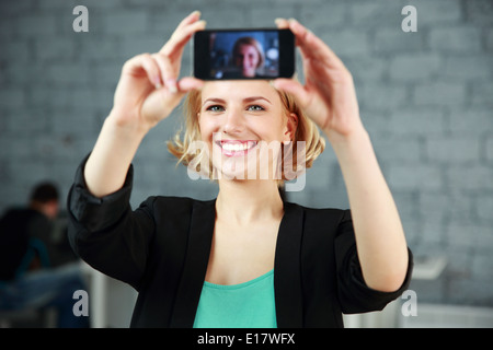 Jeune femme heureuse de prendre une photo de soi par son smartphone in office Banque D'Images