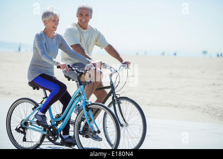 Senior couple riding bicycles on beach boardwalk Banque D'Images