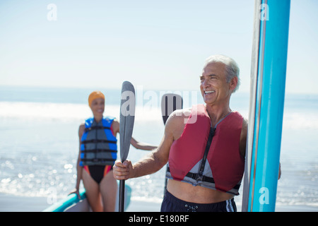 Senior couple with paddleboards on beach Banque D'Images