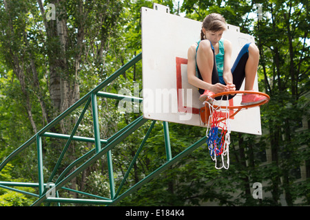 La fixation d'une jeune fille agile sur un terrain de basket-ball net Montant du but qui est posée sur le cercle de métal en le fixant avec ses mains Banque D'Images