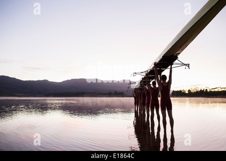 L'équipe d'aviron dans le lac à l'aube avec scull overhead Banque D'Images