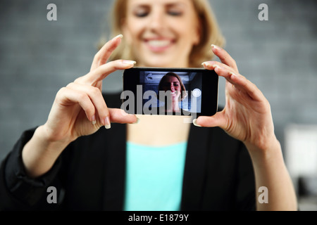 Young smiling woman making a self de par son smartphone à l'office. L'accent sur le smartphone. Banque D'Images