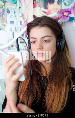 Teenage girl écouter de la musique avec des écouteurs sur son iphone sur son lit dans la chambre à coucher. Banque D'Images