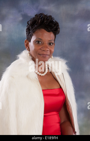 Jolie femme noire en robe rouge et blanc manteau de fourrure, souriant à la caméra avec un sourire heureux, amical Banque D'Images