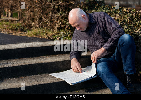 Man sitting on steps reading a newspaper Banque D'Images