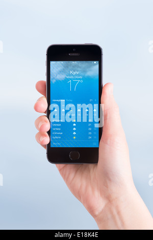 Femme tenant un tout nouveau Apple iPhone 5S avec l'application de prévisions météorologiques pour la ville de Kiev Banque D'Images