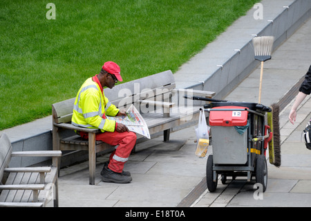 Londres, Angleterre, Royaume-Uni. Balayeuse lire un journal sur un banc Banque D'Images