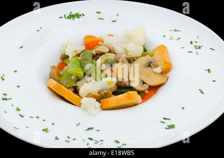 Ragoût de légumes de printemps dans une assiette blanche sur fond noir. Banque D'Images