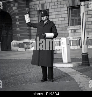 Années 1960, historique, un policier britannique portant un casque, un pardessus, des gants et avec des bandes blanches sur sa manche, faisant des signaux à la main dans une rue de Londres, Angleterre, Royaume-Uni. Banque D'Images