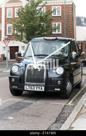 Un taxi noir London taxi avec rubans de décoration de mariage blanc attaché à l'extérieur un lieu de mariage. Banque D'Images