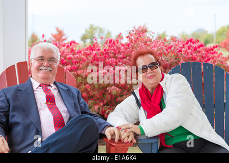 Heureux et romantic senior couple smiling at vous avez réellement, assis sur des chaises de plage automne fois et le brûlage des buissons derrière eux Banque D'Images