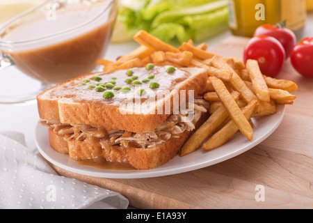 Un délicieux sandwich à la dinde sauce chaude, petits pois et frites. Banque D'Images