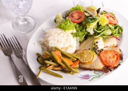 Le poisson Tilapia cuit avec les câpres, le citron et les tomates et servi dans une assiette de légumes et riz pilaf Banque D'Images