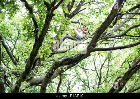 Jeune femme couchée en haut des branches d'arbres en relaxant partiellement masquée par les feuilles Banque D'Images