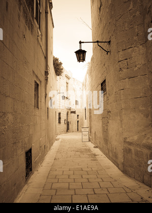 Une voix monotone, sépia vue d'une étroite rue médiévale de Mdina, Malte. L'ancienne capitale de Malte, Mdina, également connu sous le nom de la ville silencieuse. Banque D'Images