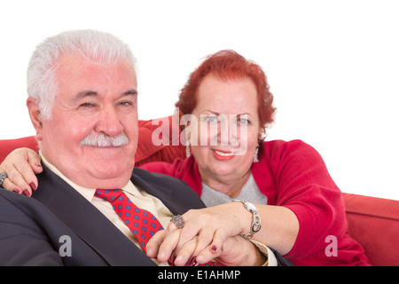 Romantic couple assis près l'un de l'autre tenant la main sur un canapé rouge et regardant la caméra avec satisfait friendly Banque D'Images