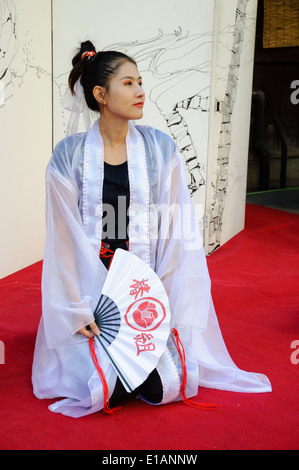 Jeune femme d'origine asiatique interprète en costume traditionnel s'agenouille sur scène lors d'une performance Banque D'Images