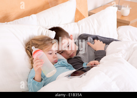 Assez petit frère et soeur d'aller dormir près de concert dans une ambiance chaleureuse confortable lit avec une tablette ordinateur sur lequel e Banque D'Images