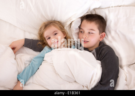 Jeune garçon de protection au lit avec sa petite sœur qui veille sur elle pendant qu'elle se trouve de l'appareil photo alors qu'ils préparent Banque D'Images