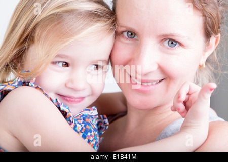 Belle mère heureuse et sa petite fille souriant à la caméra en tant qu'ils s'embrassent dans une étreinte aimante Banque D'Images
