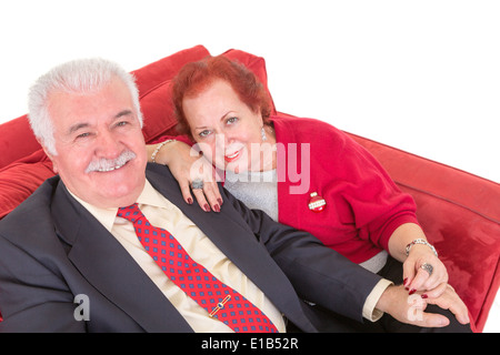 Couple assis sur un confortable canapé rouge affectueusement la main et à la recherche jusqu'à l'appareil photo avec sourires amicaux Banque D'Images
