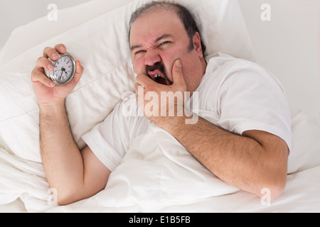 Homme souffrant d'insomnie au lit serrant son réveil alors qu'il vérifie le temps et se demande s'il va se réveiller à la m Banque D'Images