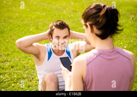 L'homme de faire des sit-ups tout en femme est de regarder l'heure de l'exercice sur téléphone mobile Banque D'Images