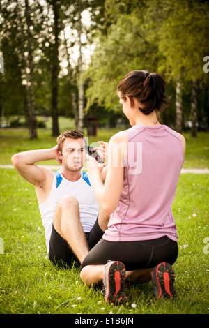 L'homme de faire des sit-ups tout en femme est de regarder l'heure de l'exercice sur téléphone mobile Banque D'Images