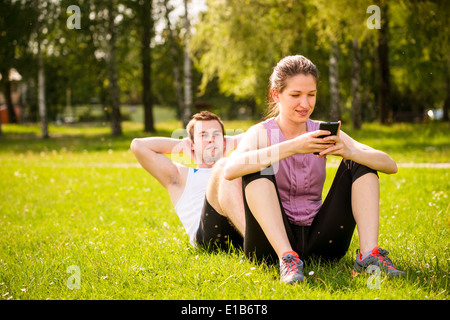 L'homme de faire des sit-ups tout en femme est assis sur ses pieds et jouer avec un téléphone mobile Banque D'Images