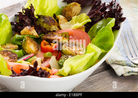 Bol de salade verte à feuilles en bonne santé avec les dés de tomates, choux de bruxelles sautés et radis servi dans un plat prêt pour un déli Banque D'Images