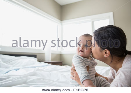 Mother kissing baby on bed
