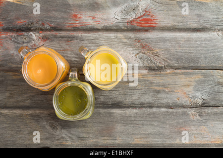 Mangue tropicale rafraîchissante saine orange kiwi jus de fruits servis dans trois verseuses en verre sur une vieille table de pique-nique en bois patiné Banque D'Images