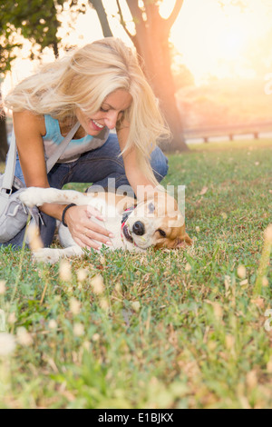 Pretty smiling blonde woman en jeans mentir et jouer avec chien sur l'herbe Banque D'Images