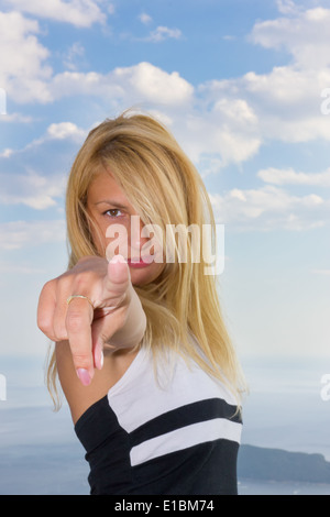 Jeune femme blonde en pointant un doigt à l'appareil photo avec ciel bleu derrière Banque D'Images