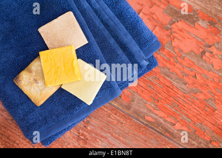 Barres de savon à base de plantes biologiques avec des extraits de plantes sur une serviette bleu frais propres vus du dessus sur une table en bois rustique w Banque D'Images