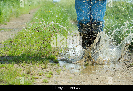 L'homme en bottes de sauter dans une flaque d'eau sur une piste dans la campagne anglaise Banque D'Images