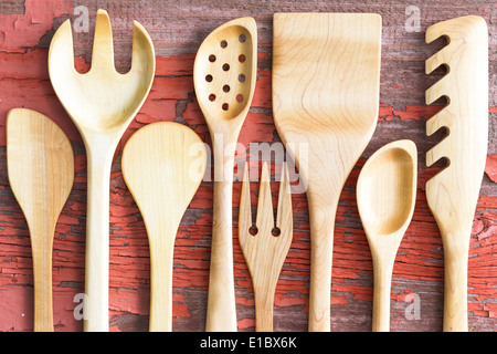 Ensemble d'ustensiles de cuisine fabriqués en bois disposées dans une rangée sur un pur grungy table de pique-nique en bois avec peinture craquelée includi rouge Banque D'Images