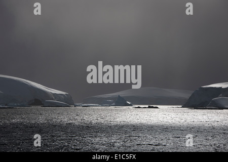 Les nuages sombres de l'approche d'une tempête, et de la lumière du soleil qui se reflète sur l'eau. Les icebergs flottant sur l'eau. Banque D'Images