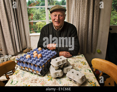 Un fermier assis à une table dans une ferme avec des plateaux d'œufs frais. Banque D'Images