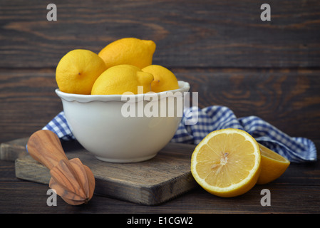 Les citrons dans un bol blanc avec l'alésoir de citron sur fond de bois Banque D'Images