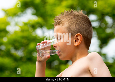 Young caucasian boy drinking from glass avec de l'eau douce en plein air en été. Banque D'Images