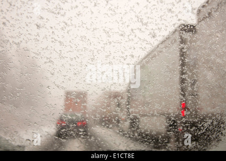 Les voitures et les camions roulant sur les routes neige prises à travers un pare-brise couvert de flocons de neige. Banque D'Images